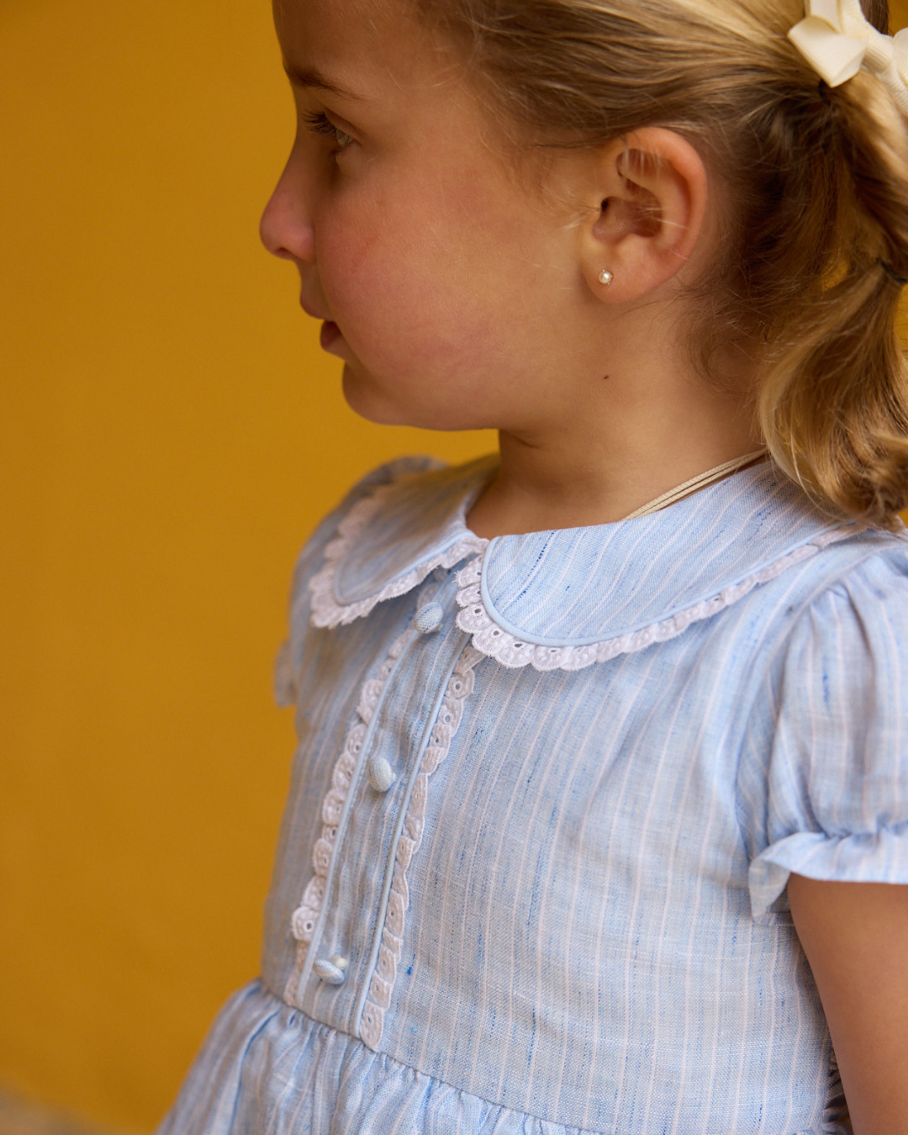 Young girl wearing a light blue dress with a lace collar against a yellow background