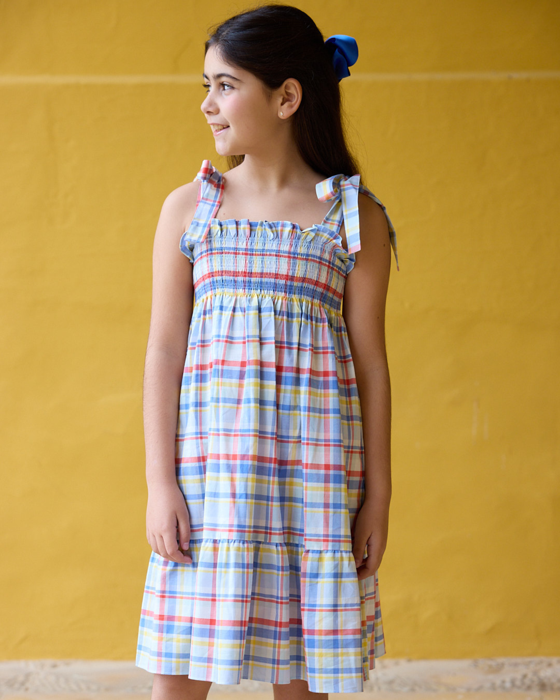 Young girl wearing a plaid dress against a yellow background