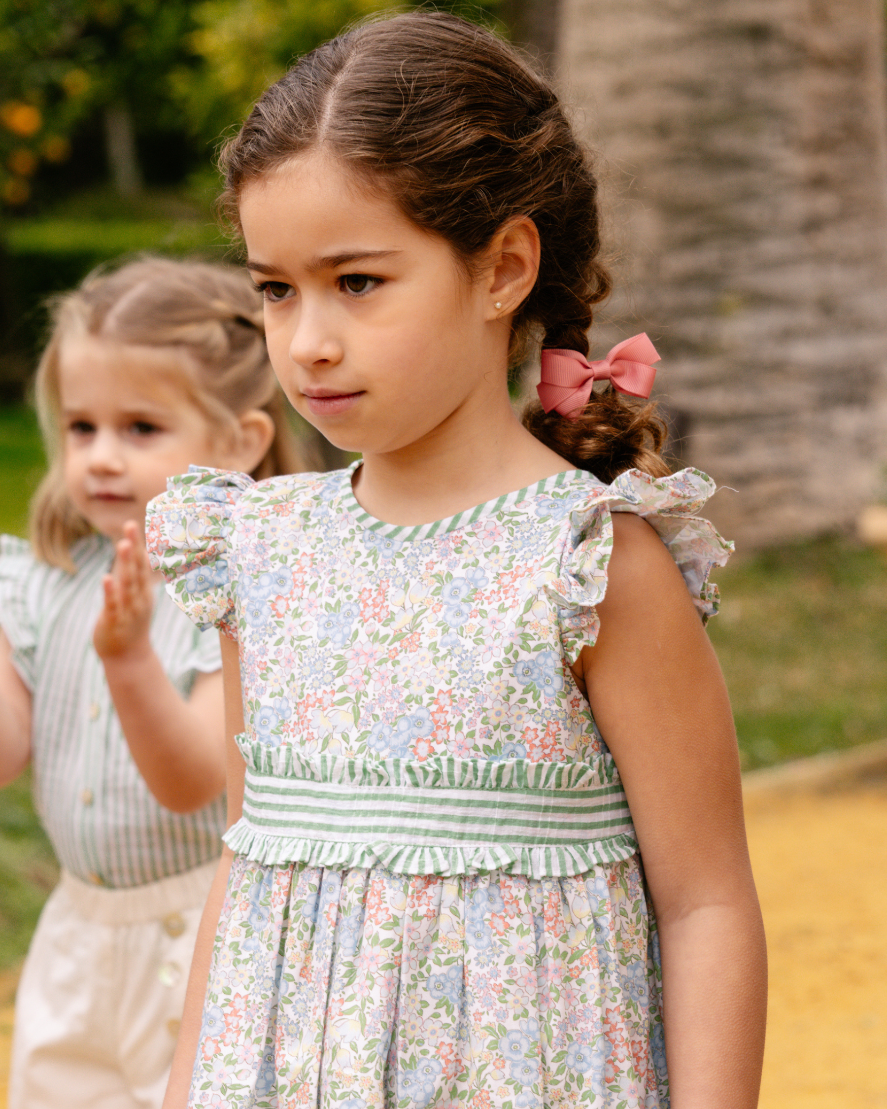 Two young girls in floral dresses standing outdoors with a blurred background