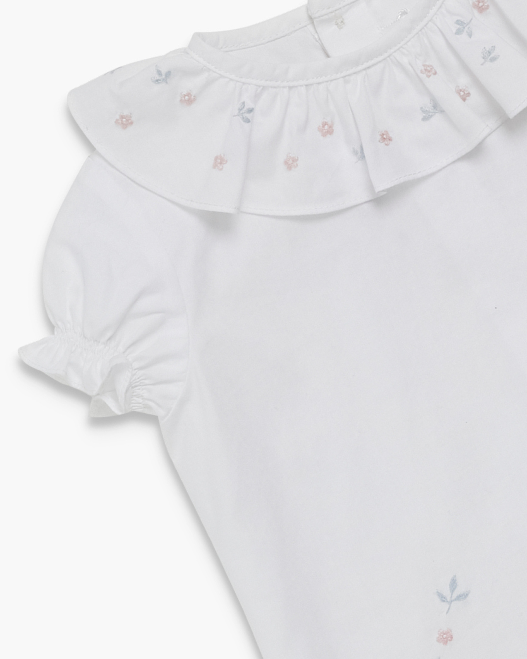 White baby romper with ruffled collar and floral embroidery on a white background