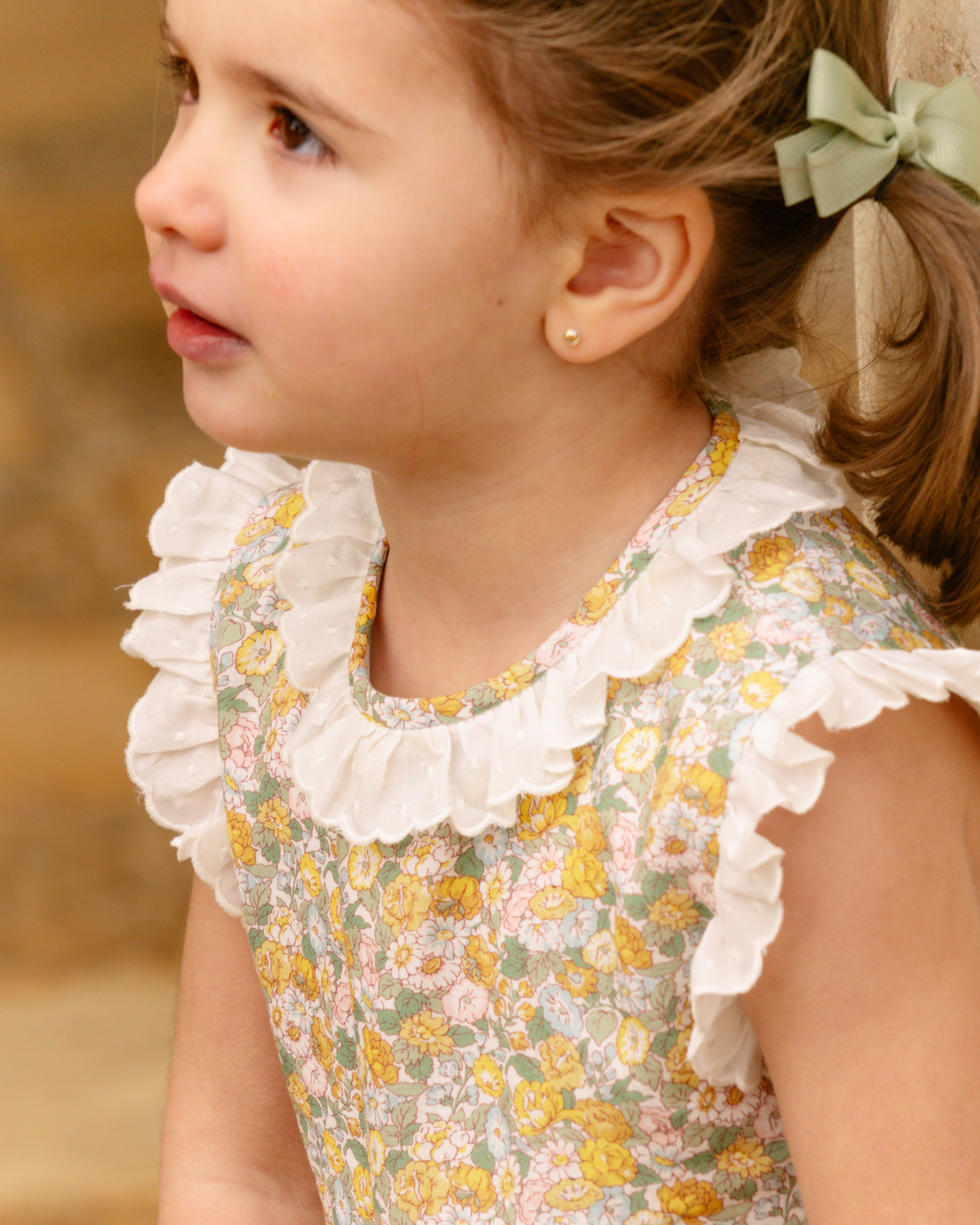 Close-up of a young girl wearing a floral dress with ruffled collar.