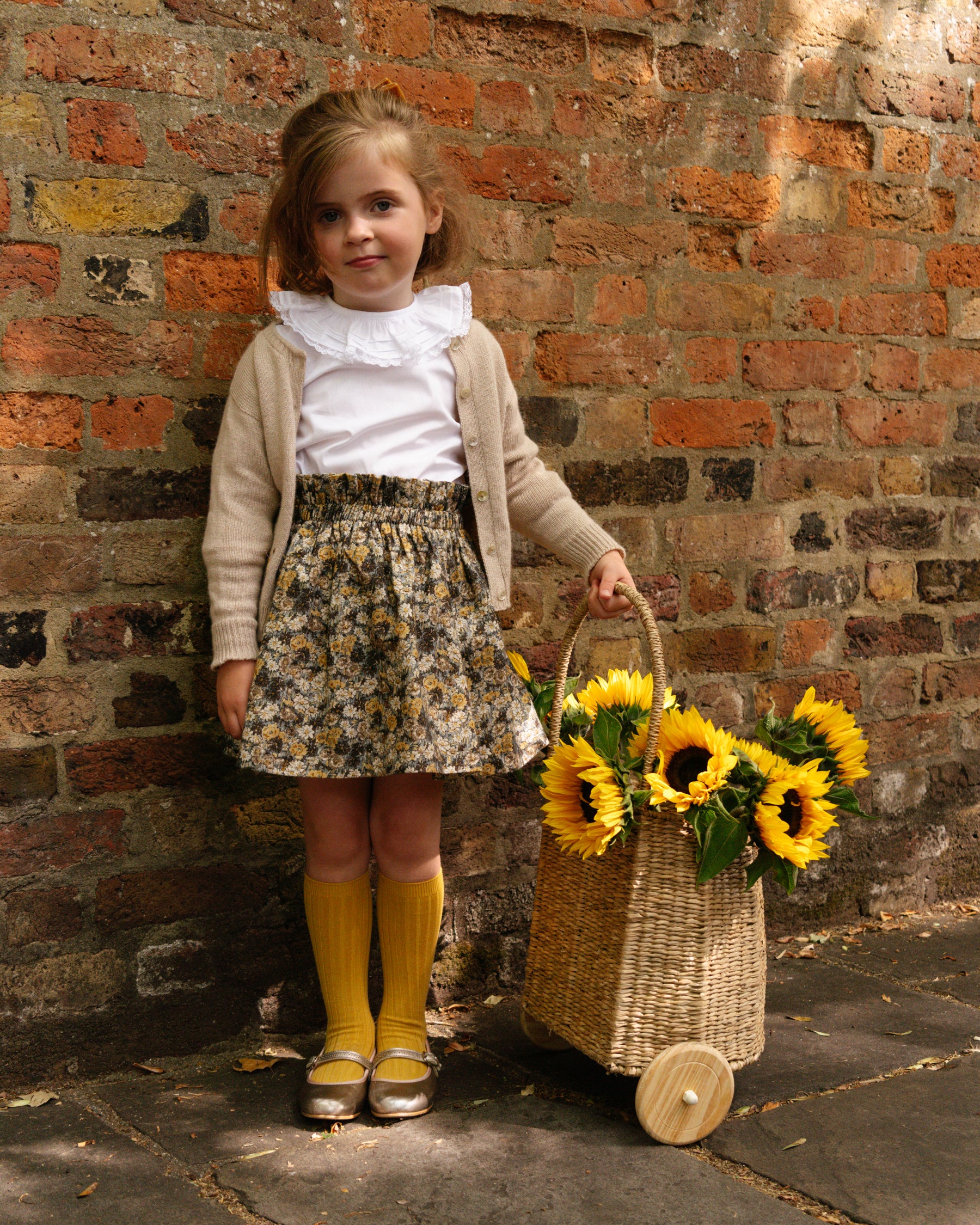 Young girl holding a basket of sunflowers against a brick wall.