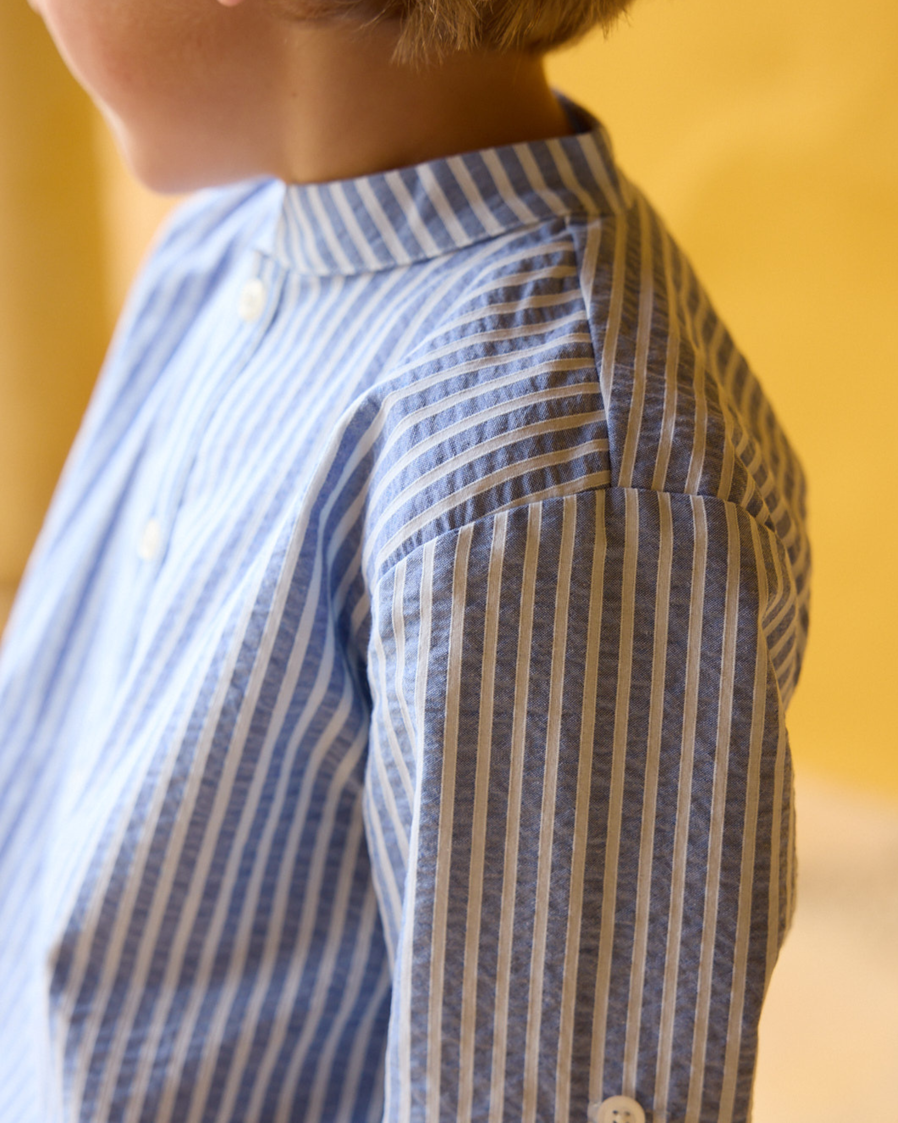 Close-up of a person wearing a blue and white striped shirt against a blurred yellow background