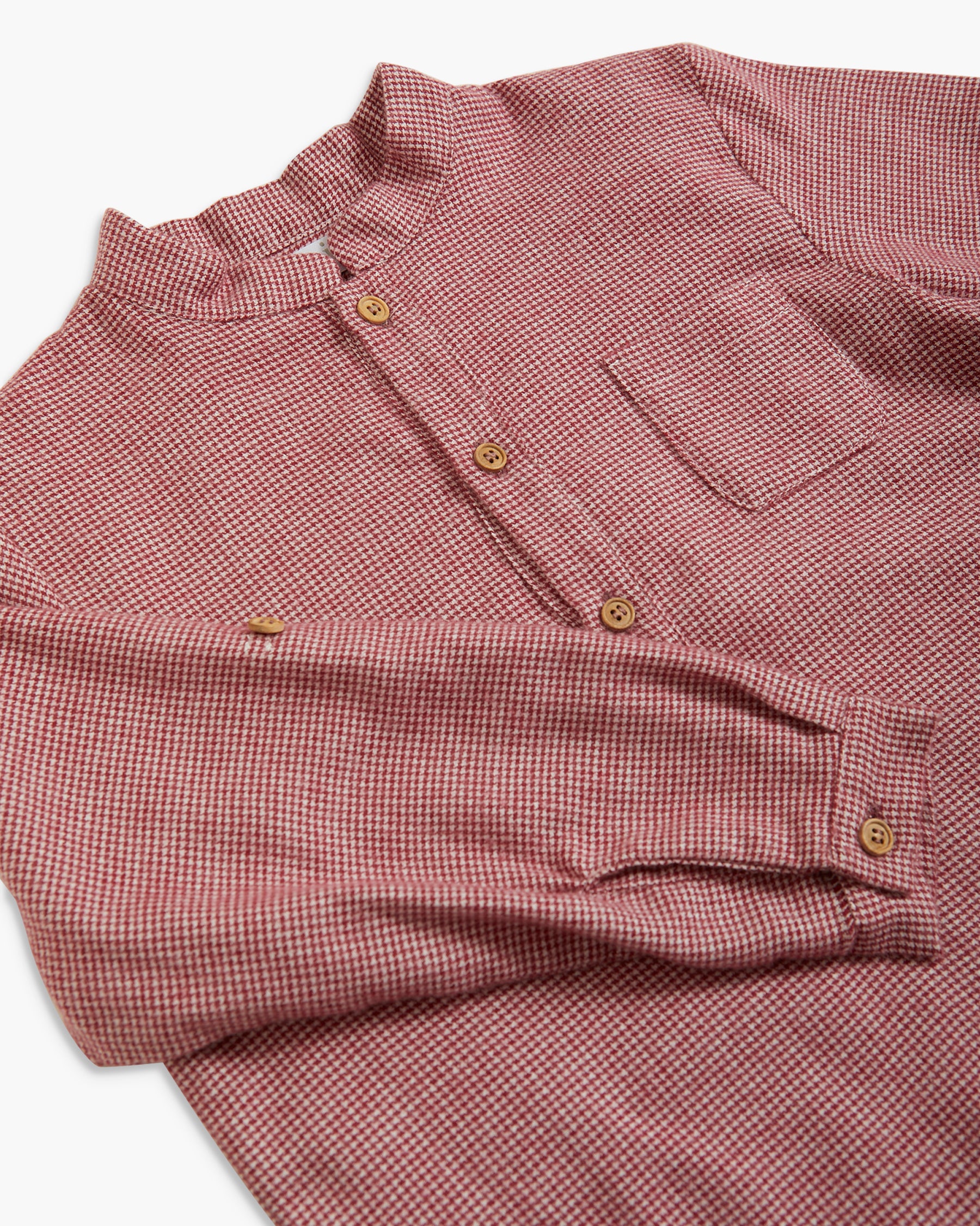 A close-up of a long-sleeve button-up shirt with a small-scale red and white gingham pattern, featuring brown buttons and a chest pocket.