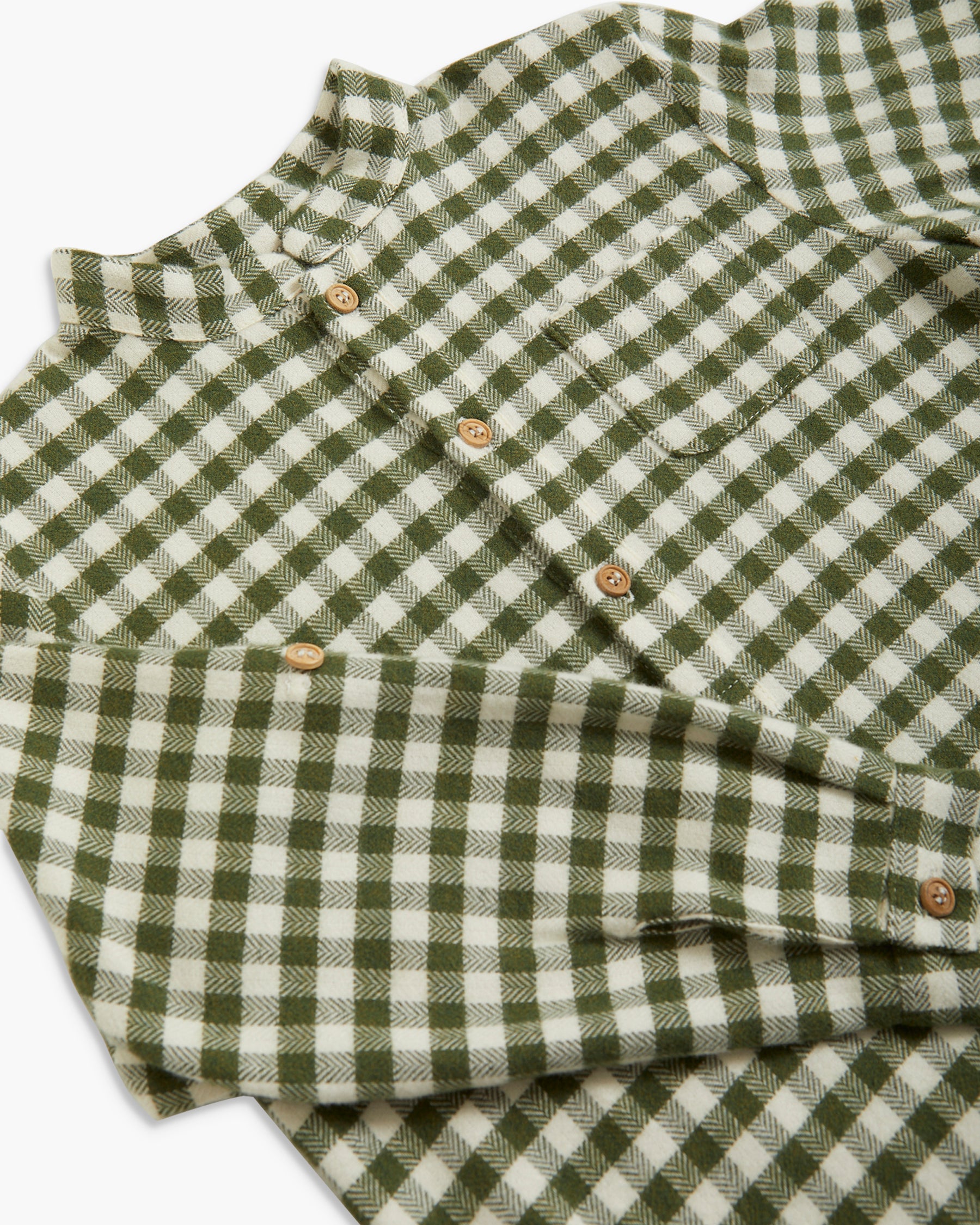 A close-up of a green and off-white gingham plaid button-up shirt, folded to show the fabric texture and check pattern, with light brown buttons.