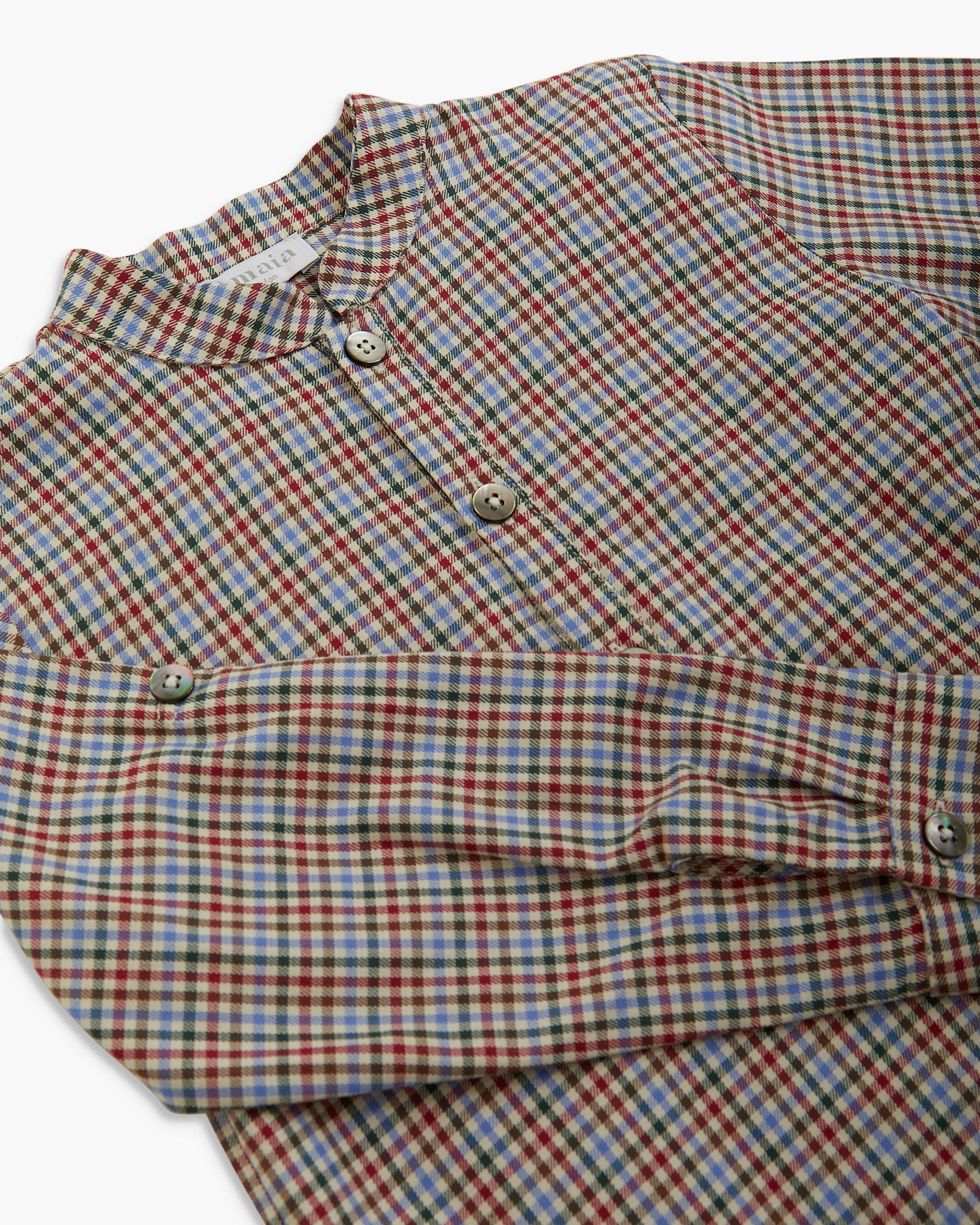 A close-up of a long-sleeve button-up shirt with a small check pattern in red, blue, and white, laid flat on a white background.