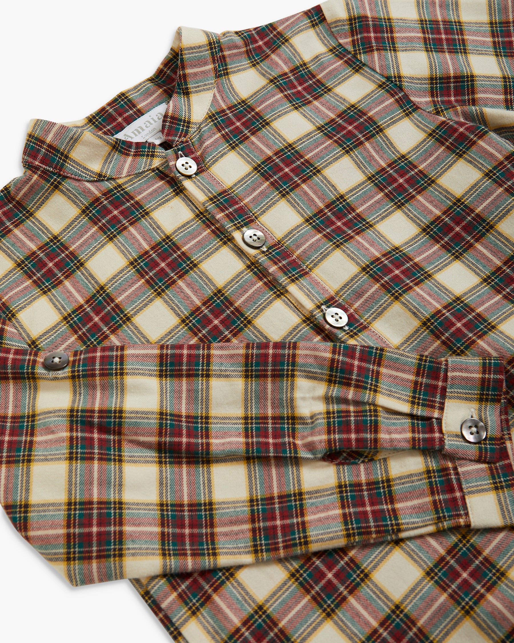 A close-up of a plaid button-up shirt in a cream, red, green, and yellow tartan pattern, with visible buttons and a folded cuff.