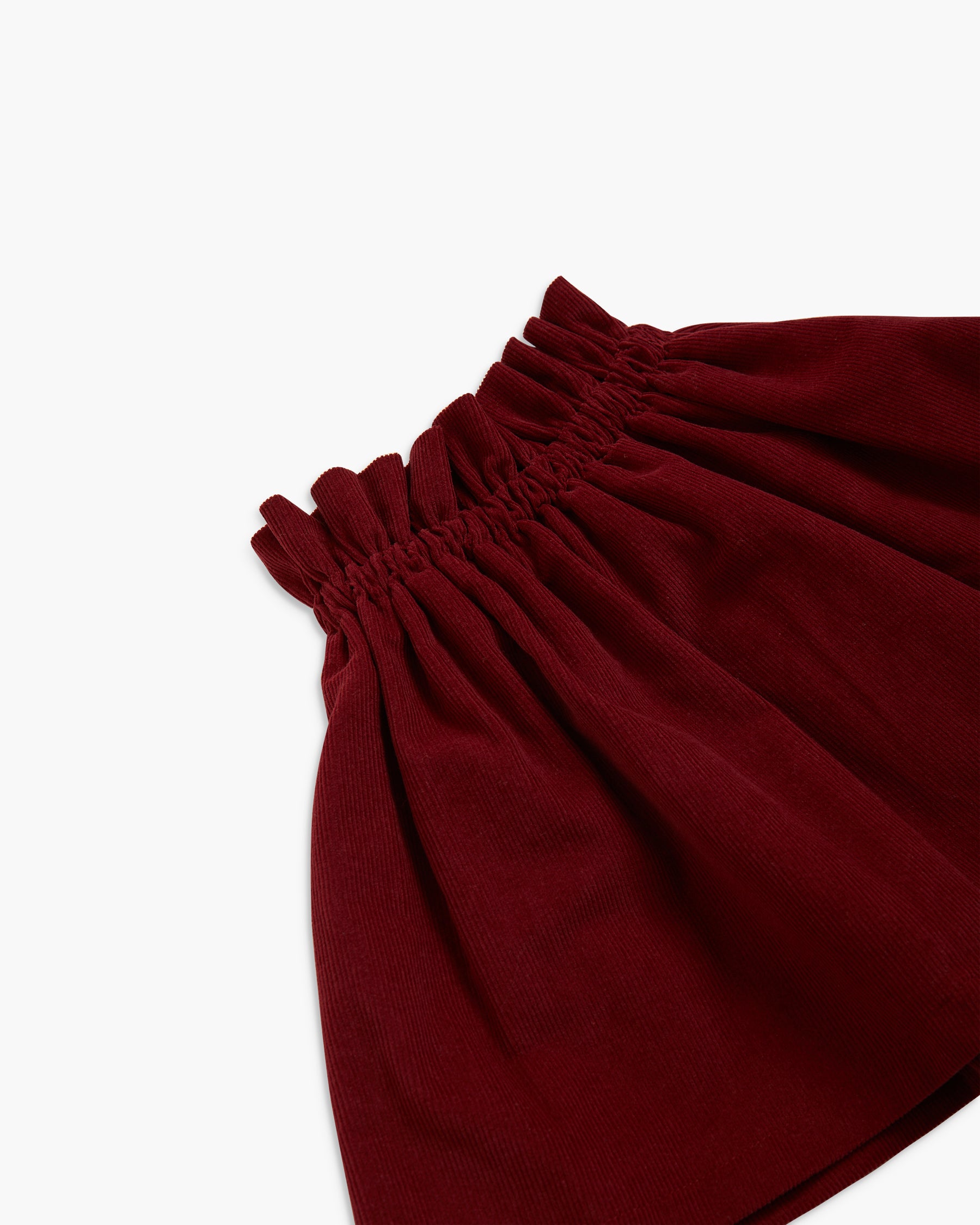 Close-up of a dark burgundy fabric garment with a gathered elastic waistband, shown against a plain white background.