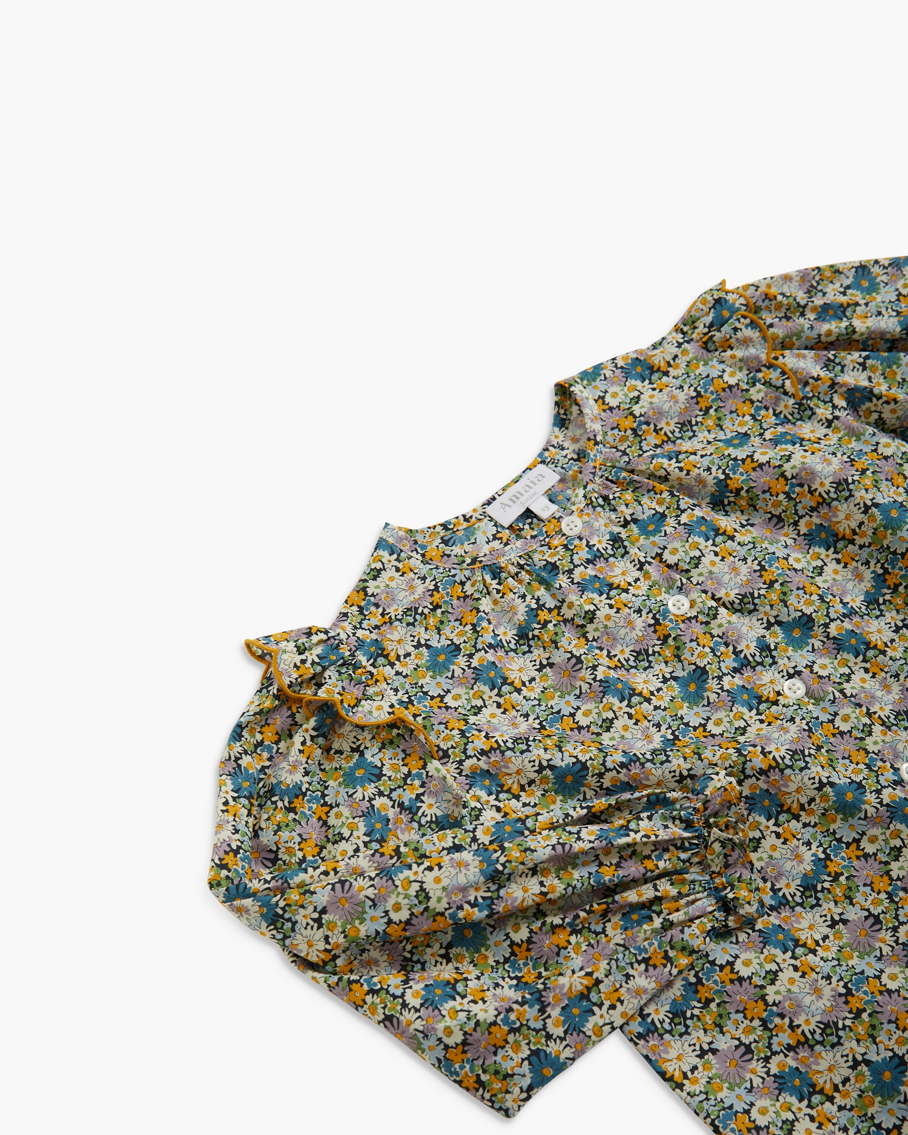 A close-up of a floral-patterned blouse with ruffled sleeves, featuring a dense print of yellow, blue, white, and green flowers on a muted grayish-blue background.