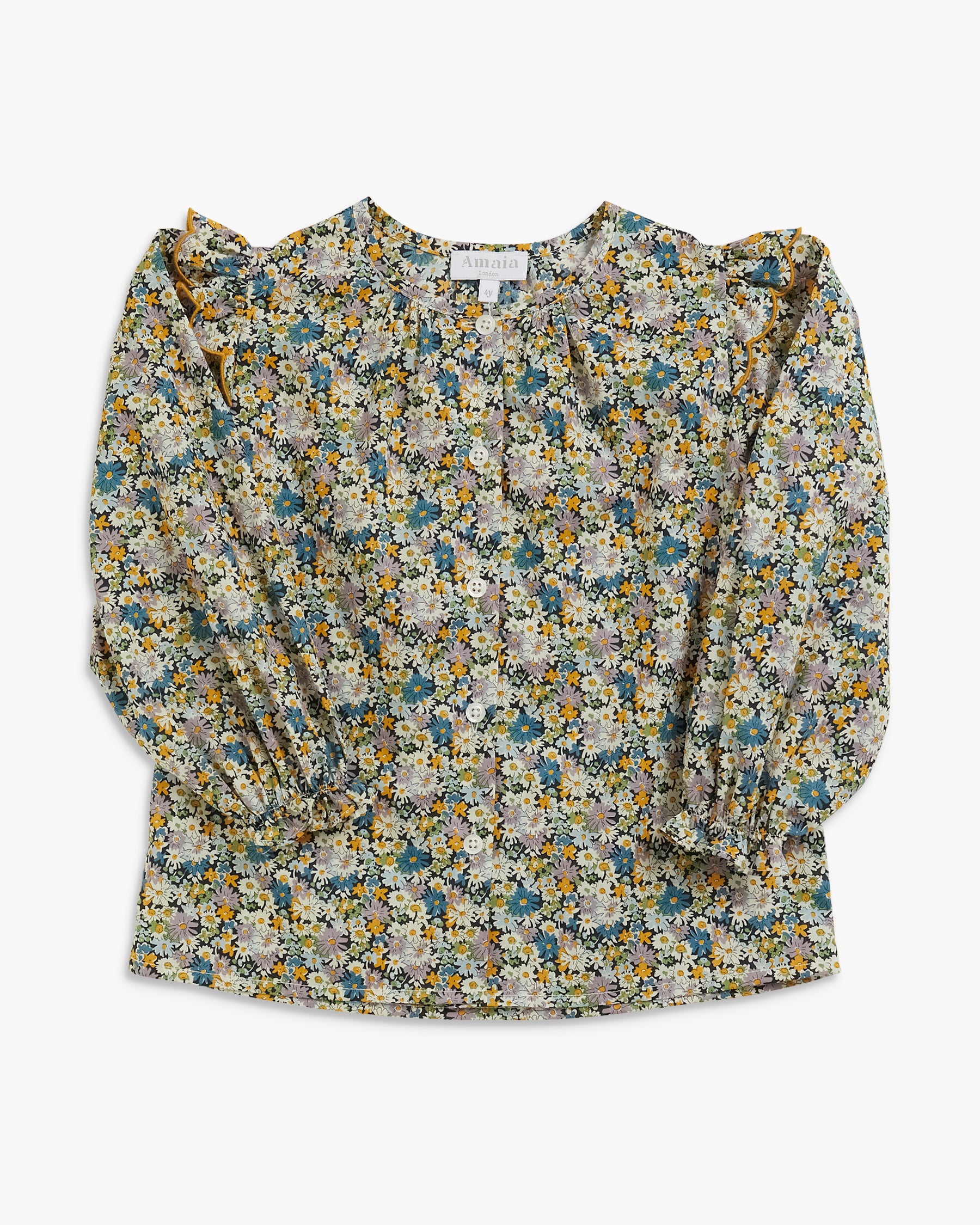 A long-sleeve blouse with a dense floral print in muted blue, yellow, white, and beige tones, featuring ruffled shoulders and a gathered waist, laid flat against a light gray background.