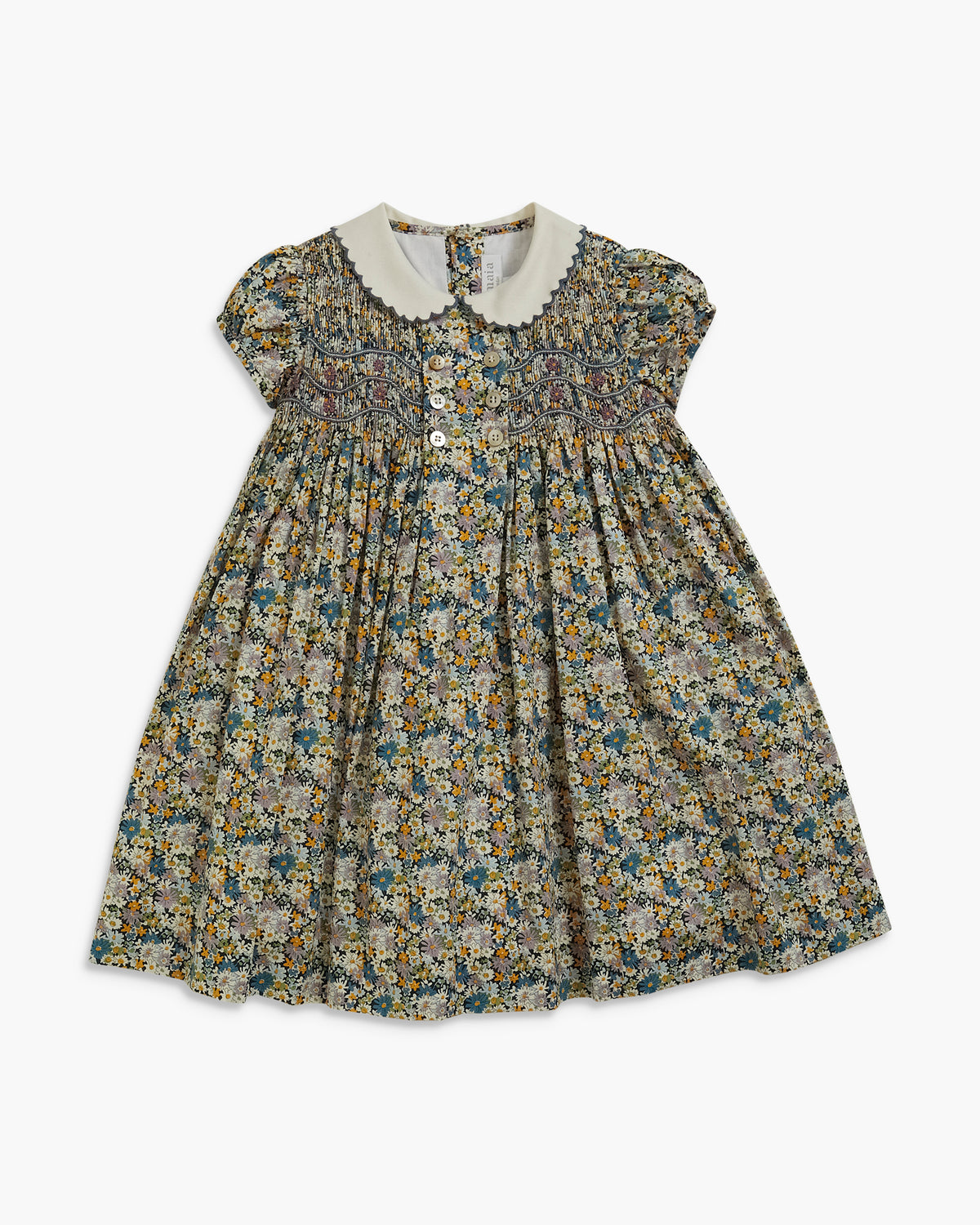 A toddler girl's short-sleeve dress with a dense floral print in muted green, blue, and yellow tones on a cream background, featuring a white scalloped Peter Pan collar and smocked bodice.