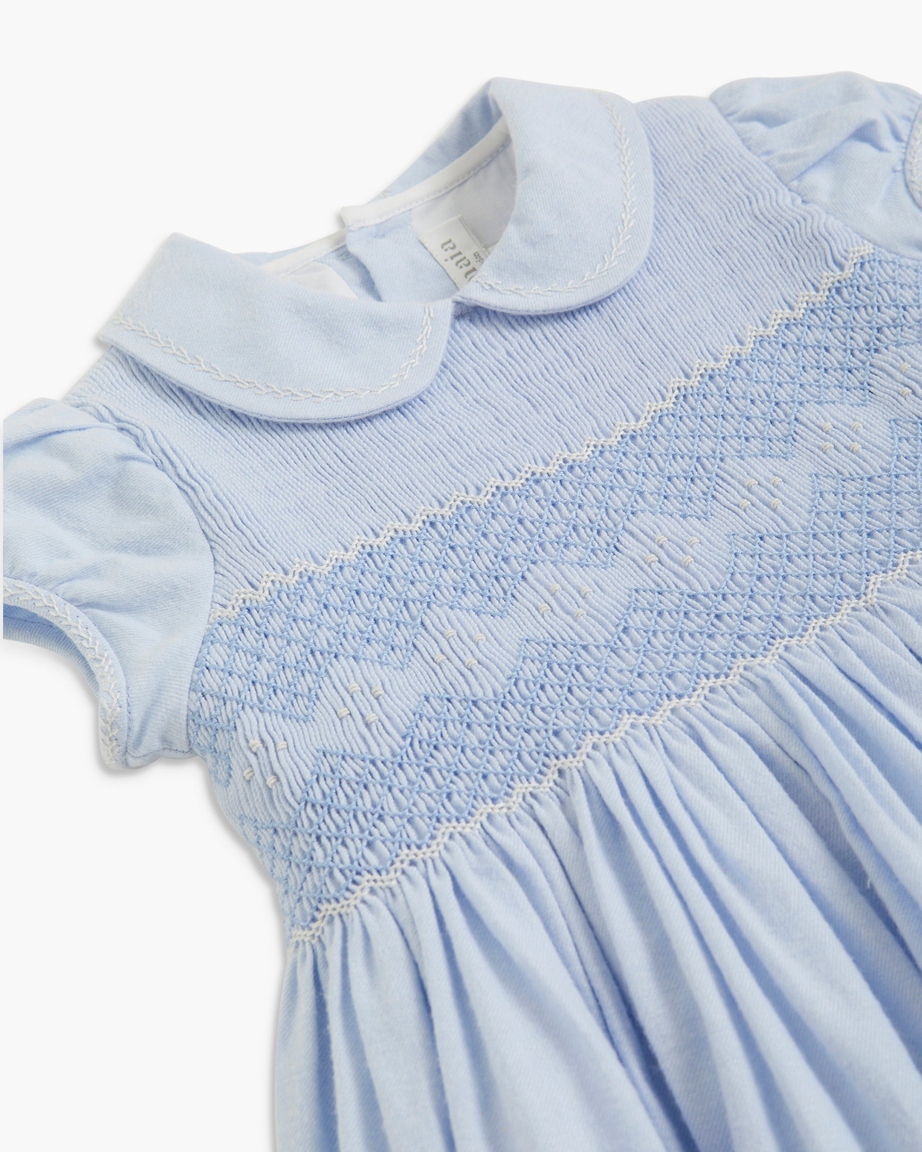 Close-up of a light blue baby dress featuring a smocked bodice with a diamond pattern, a white Peter Pan collar, and short puff sleeves.