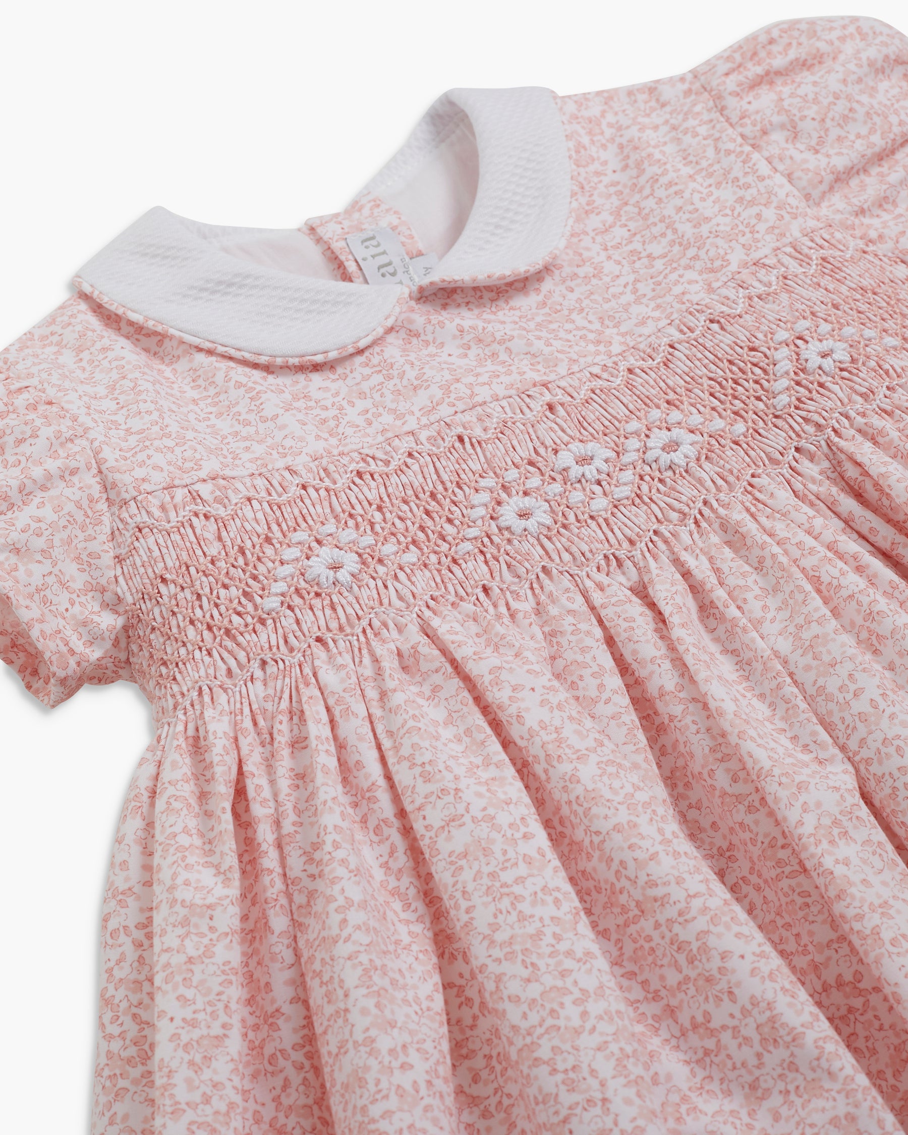 Pink smocked dress with white floral embroidery on a white background