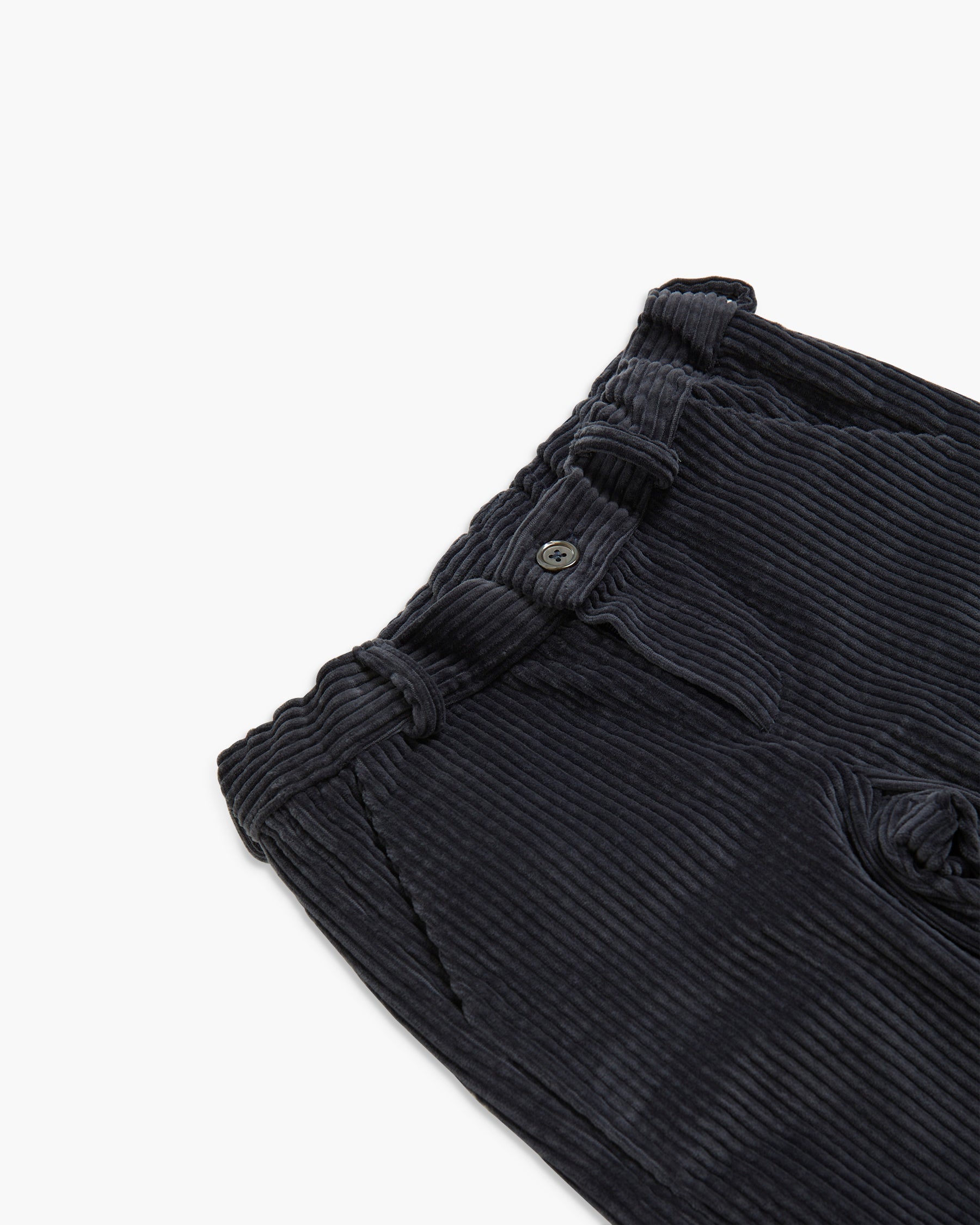 Close-up of dark charcoal corduroy trousers showing the waistband, button closure, and ribbed fabric texture on a clean white background.