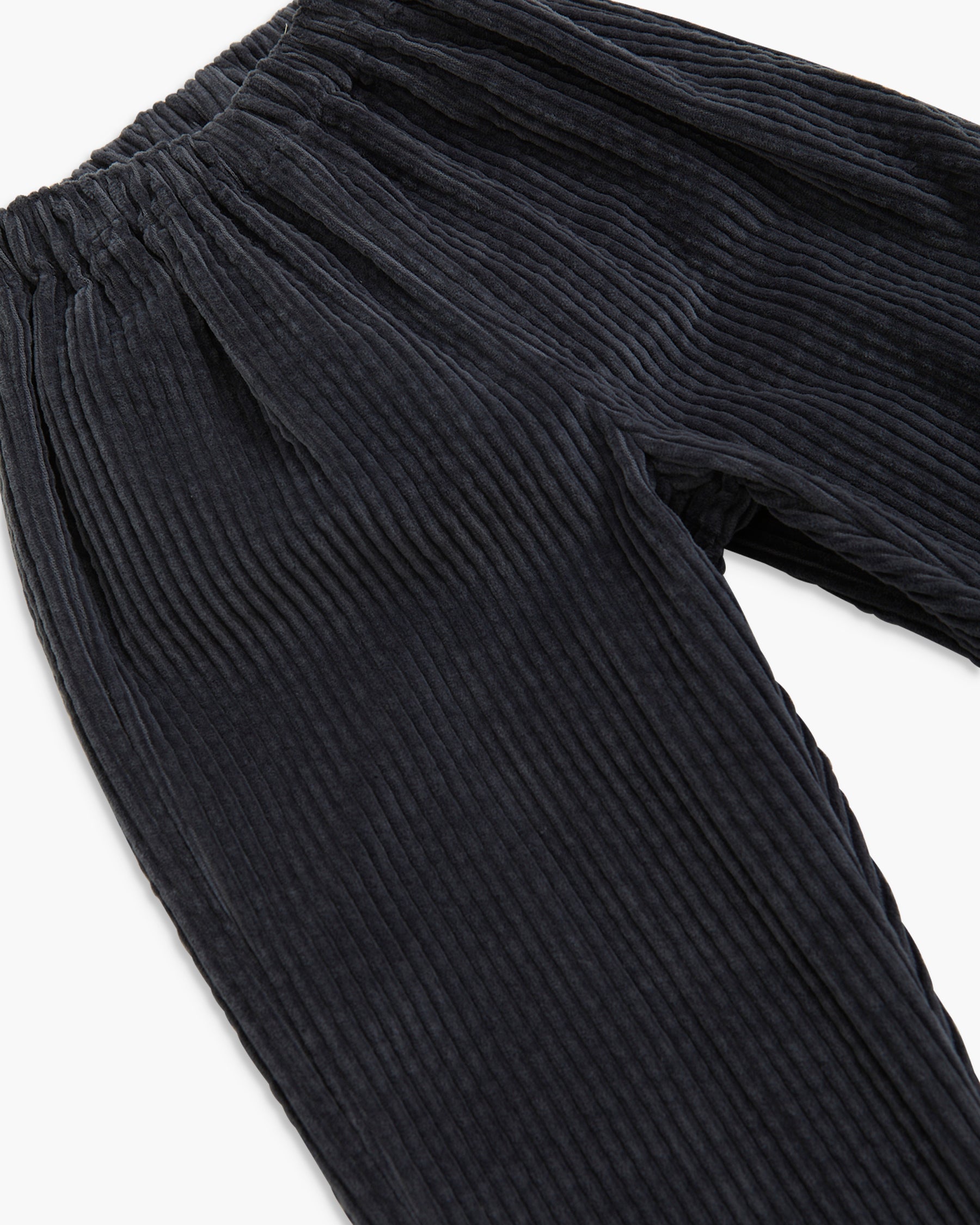 Close-up of dark charcoal corduroy pants showing the ribbed texture and elastic waistband on a white background.