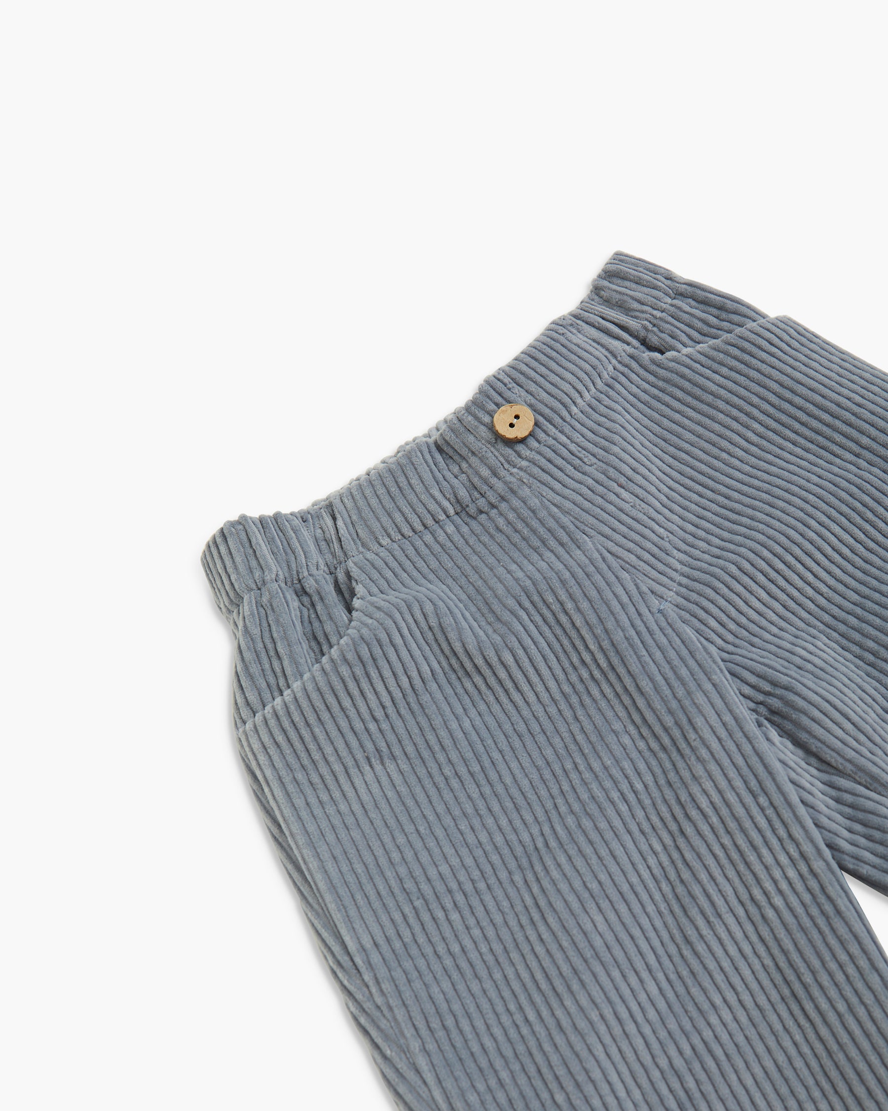 Close-up of a pair of ribbed corduroy pants in a muted blue-gray color, featuring an elastic waistband and a small wooden button closure.