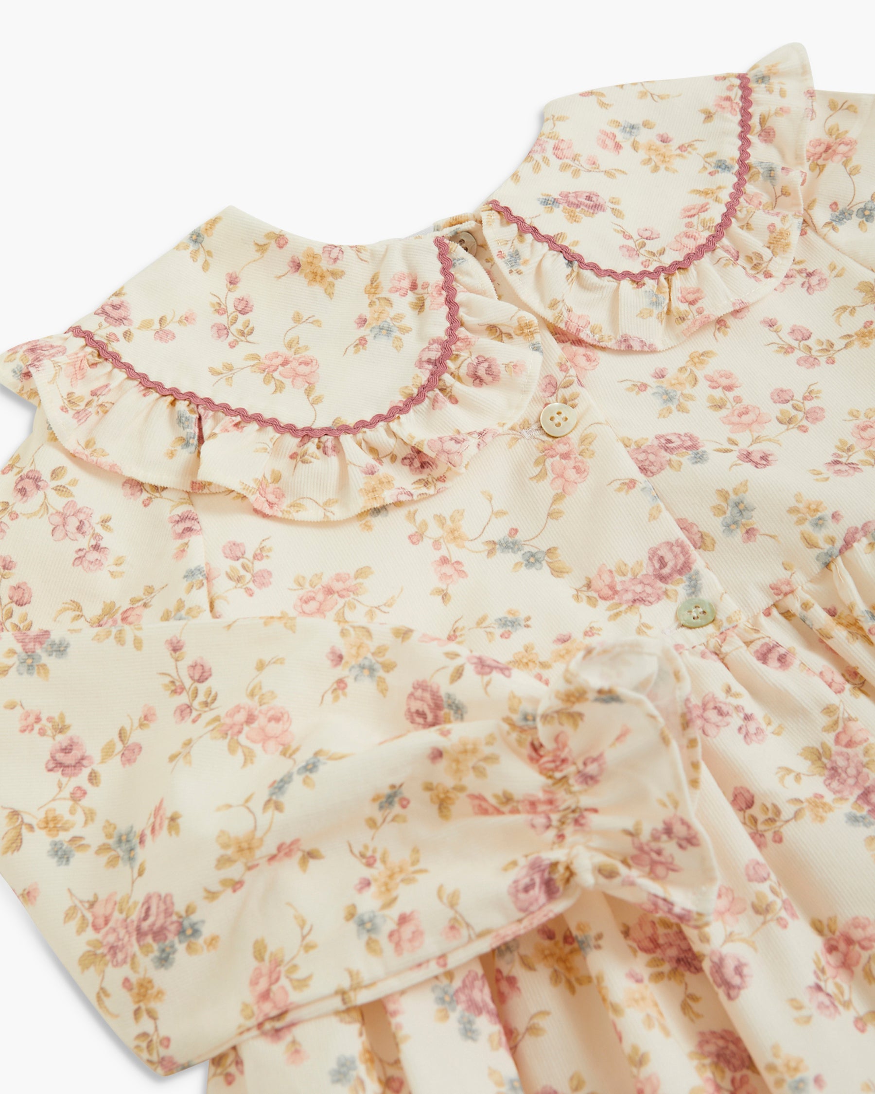 Close-up of a cream-colored floral dress with a ruffled Peter Pan collar trimmed in dusty rose, featuring a delicate floral print with pink, yellow, and blue blossoms.