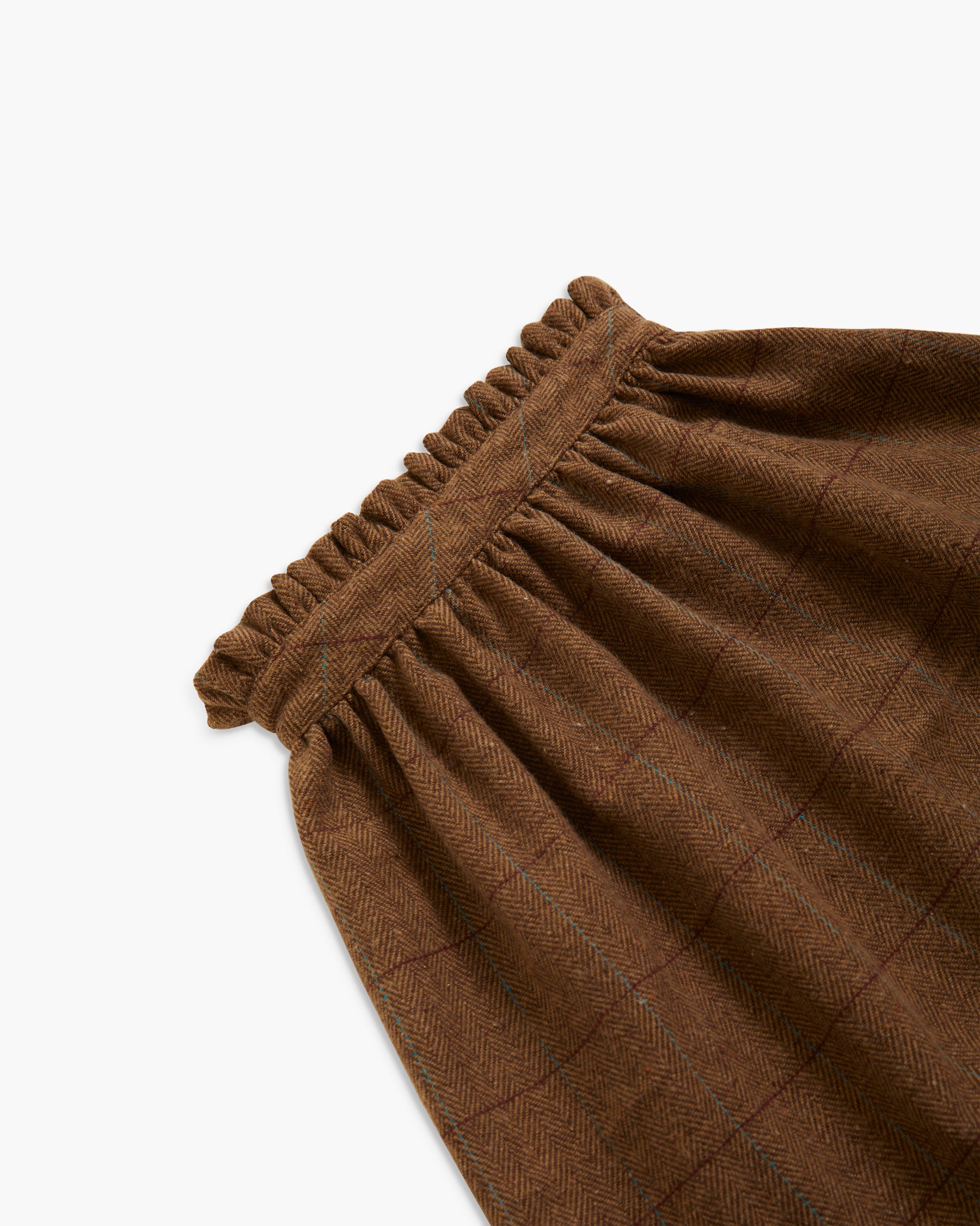 Close-up of a brown textured fabric garment with a gathered elastic waistband, showing a subtle windowpane plaid pattern on a white background.